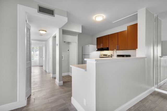 1011 Green Pine Blvd Unit G1, West Palm Beach, FL 33409 - kitchen with freestanding refrigerator, under cabinet range hood, brown cabinetry, baseboards, and light wood-style floors