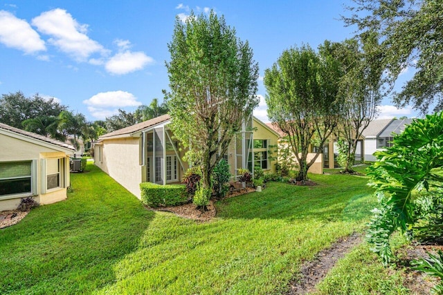 view of side of property with stucco siding, a yard, and central AC