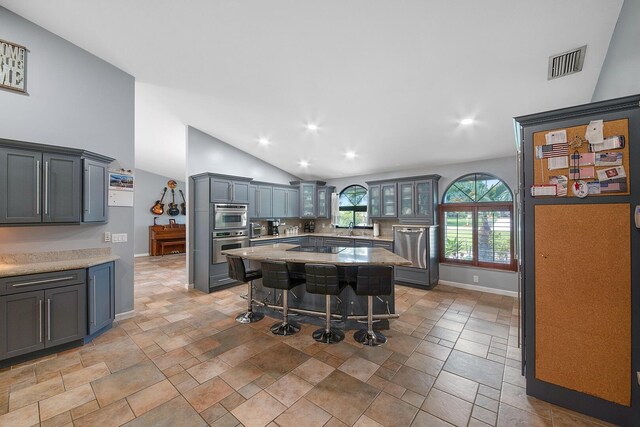 kitchen featuring stainless steel appliances, vaulted ceiling, a kitchen breakfast bar, baseboards, and a center island