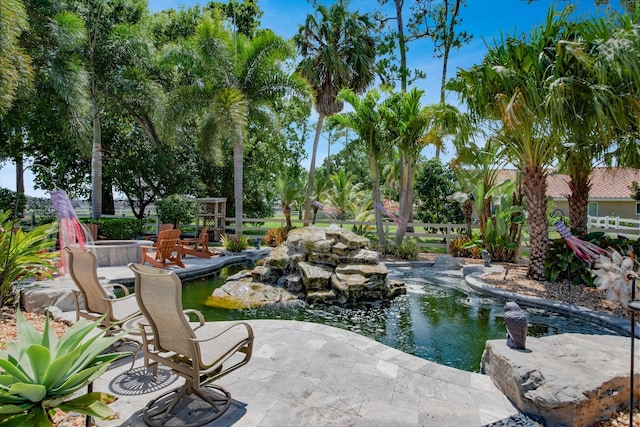 view of property's community featuring a garden pond, a patio, and fence