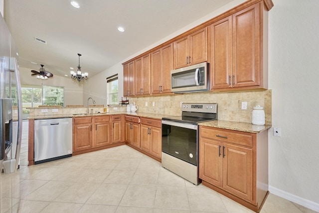 kitchen featuring stainless steel appliances, a sink, decorative backsplash, light stone countertops, and a chandelier