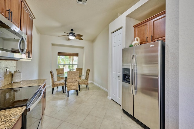 kitchen with stainless steel appliances, a ceiling fan, light tile patterned floors, light stone counters, and baseboards