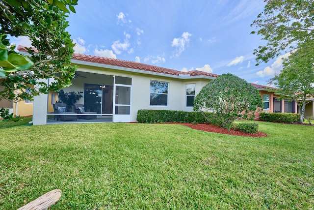 back of property featuring a sunroom, a tile roof, a lawn, and stucco siding