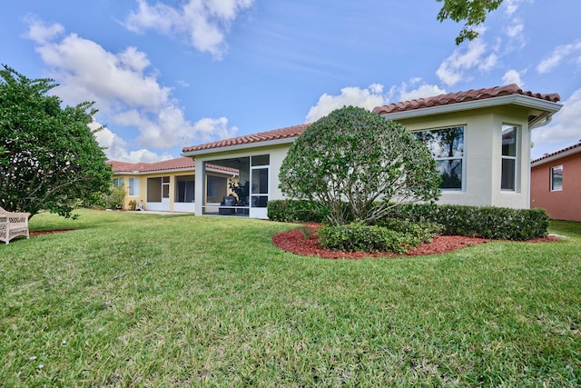 back of property featuring a tile roof, a lawn, a sunroom, and stucco siding