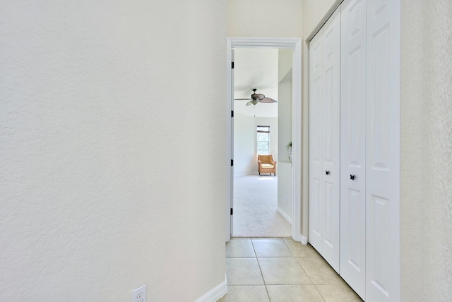 hallway with baseboards, light tile patterned flooring, and a textured wall