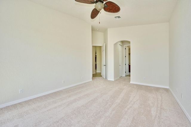 empty room with arched walkways, a ceiling fan, light colored carpet, and baseboards