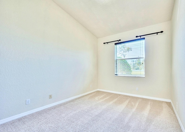 spare room featuring carpet, vaulted ceiling, and baseboards