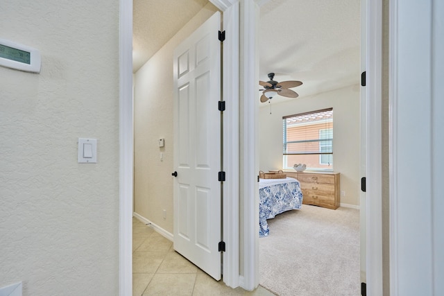 corridor featuring a textured wall, baseboards, light tile patterned floors, and a textured ceiling
