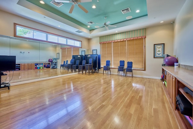 exercise room with a tray ceiling, ceiling fan, wood finished floors, baseboards, and recessed lighting