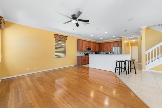 kitchen with stainless steel appliances, ceiling fan, ornamental molding, a center island with sink, and baseboards