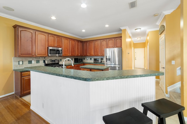 kitchen featuring appliances with stainless steel finishes, an island with sink, backsplash, crown molding, and baseboards