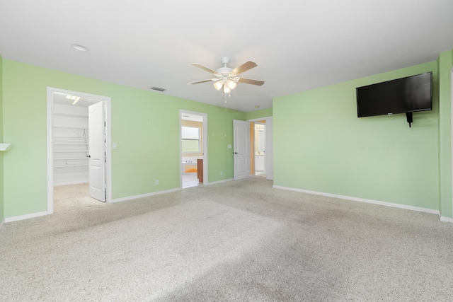 unfurnished bedroom featuring carpet, a walk in closet, baseboards, ceiling fan, and a closet