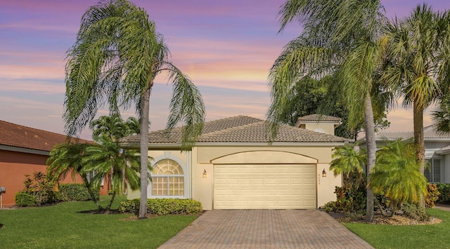 mediterranean / spanish home featuring decorative driveway, a garage, a tiled roof, a front yard, and stucco siding