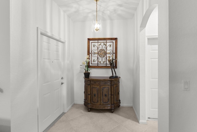 doorway with arched walkways, light tile patterned floors, and baseboards