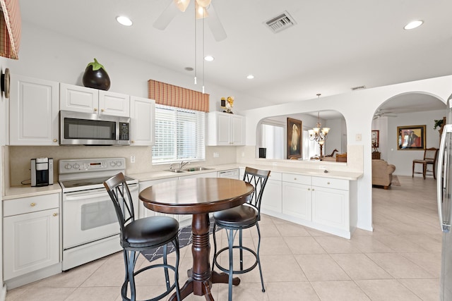 kitchen with electric stove, stainless steel microwave, a ceiling fan, arched walkways, and light countertops