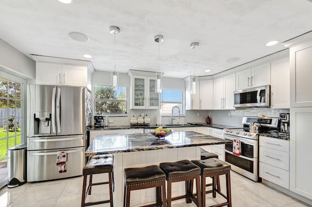 kitchen featuring appliances with stainless steel finishes, light tile patterned floors, a sink, tasteful backsplash, and white cabinets