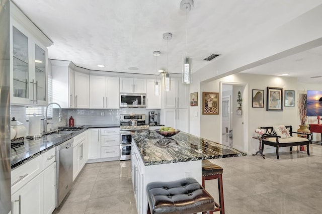 kitchen with stainless steel appliances, a sink, a kitchen breakfast bar, tasteful backsplash, and dark stone countertops