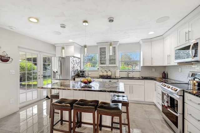 kitchen featuring appliances with stainless steel finishes, a sink, backsplash, a kitchen breakfast bar, and dark stone counters