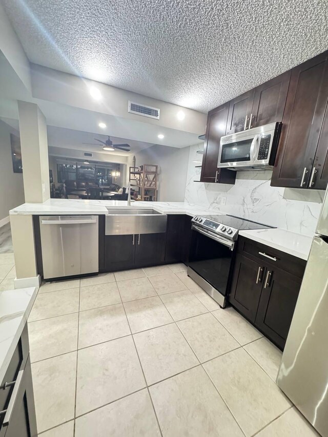 kitchen featuring stainless steel appliances, a textured ceiling, light countertops, decorative backsplash, and ceiling fan