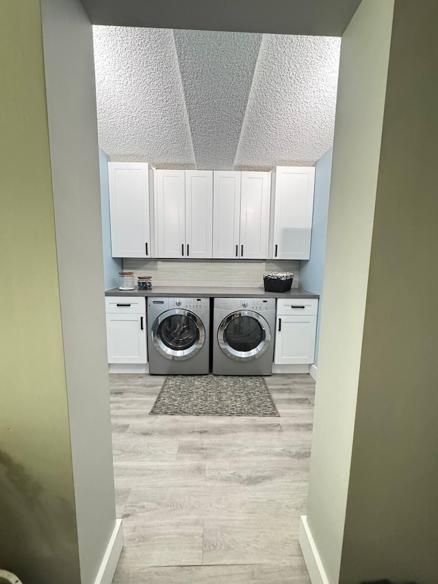 washroom featuring cabinet space, washing machine and clothes dryer, light wood-style floors, baseboards, and a textured ceiling