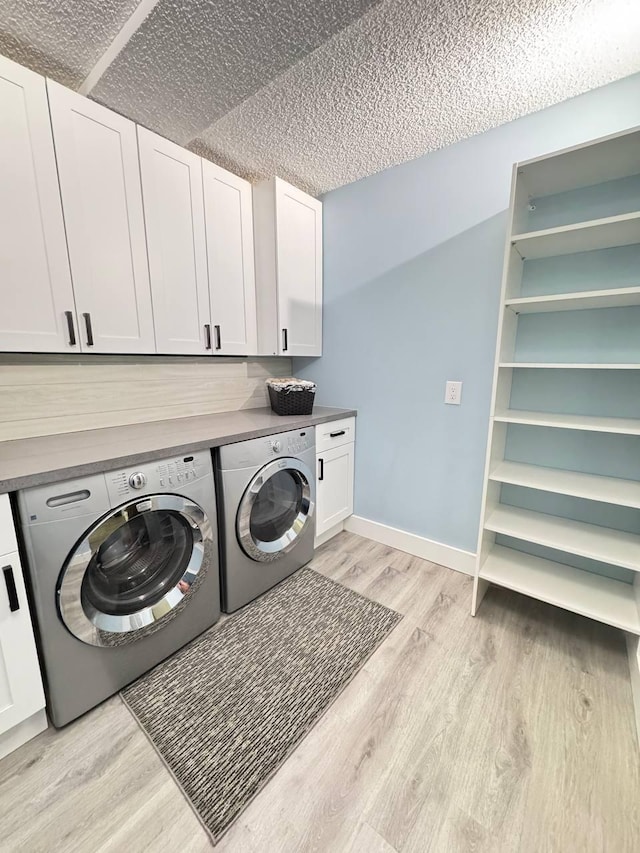 laundry area with washer and clothes dryer, light wood-style flooring, cabinet space, a textured ceiling, and baseboards