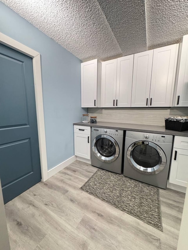 clothes washing area with cabinet space, washing machine and clothes dryer, light wood-type flooring, baseboards, and a textured ceiling