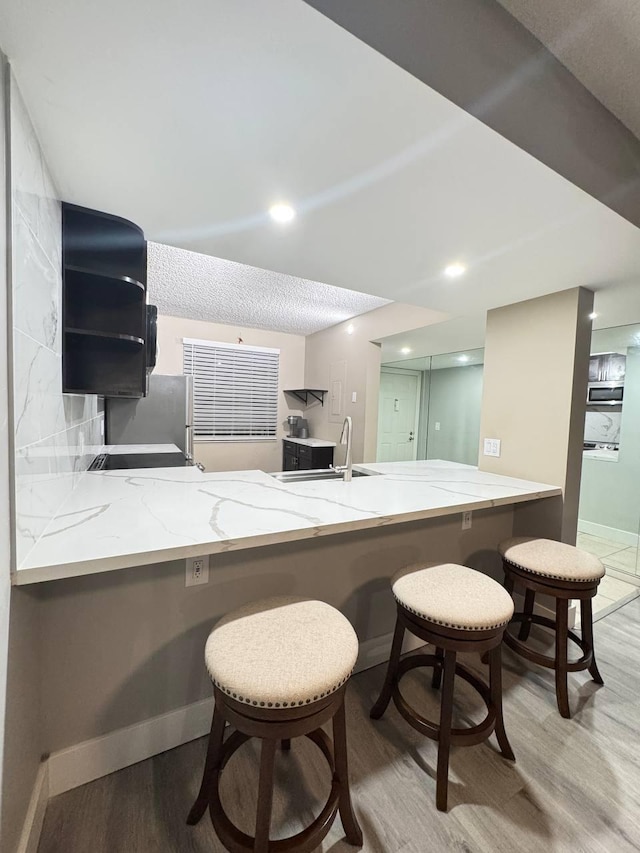 kitchen with a sink, wood finished floors, light stone countertops, a peninsula, and recessed lighting