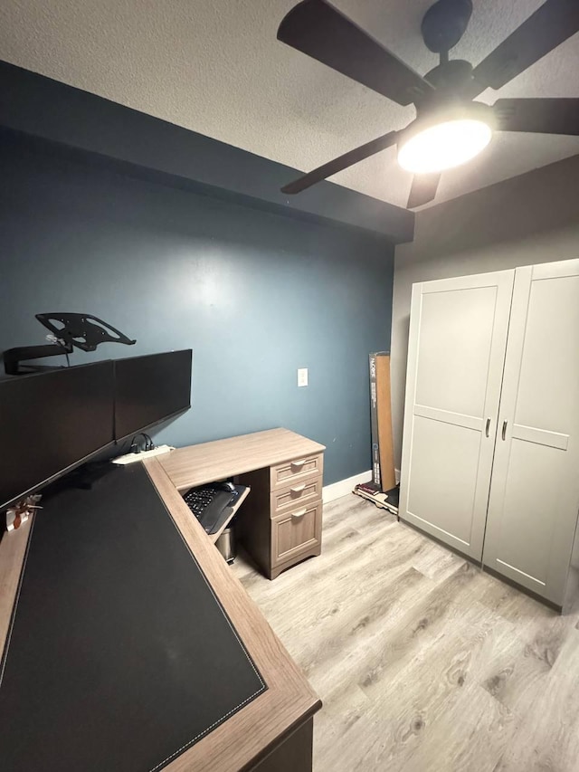 unfurnished office featuring light wood-type flooring, a textured ceiling, ceiling fan, and baseboards