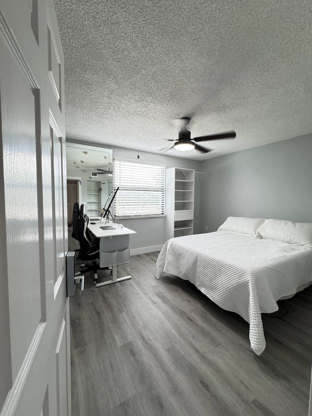 bedroom with wood finished floors, a ceiling fan, baseboards, and a textured ceiling