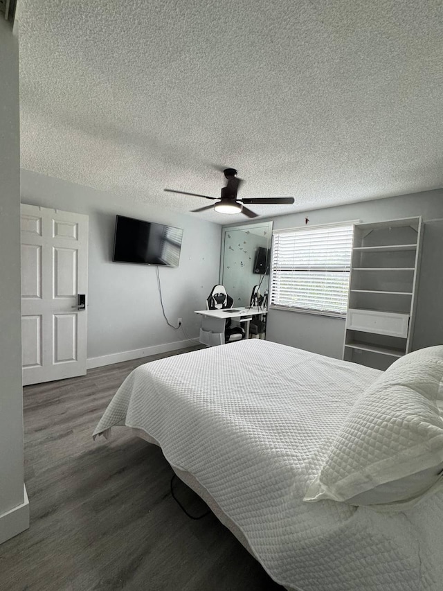 bedroom with wood finished floors, baseboards, a textured ceiling, a ceiling fan, and a desk