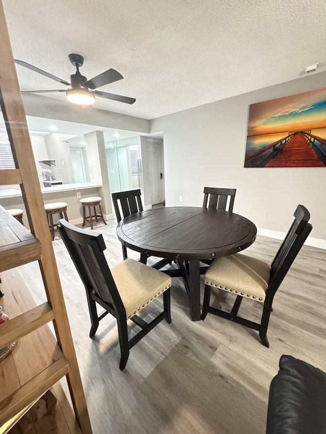 dining room with light wood-style floors, a textured ceiling, a ceiling fan, and baseboards