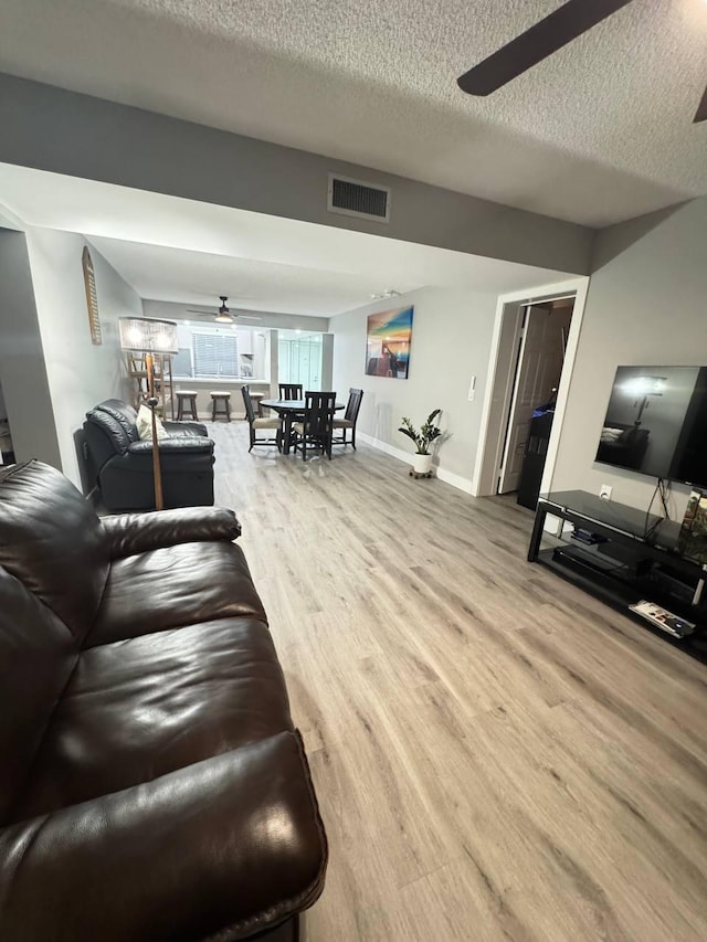 living room featuring a ceiling fan, wood finished floors, a textured ceiling, and baseboards