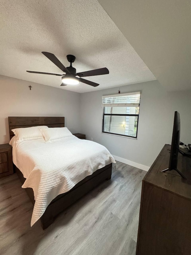 bedroom with wood finished floors, a textured ceiling, baseboards, and ceiling fan
