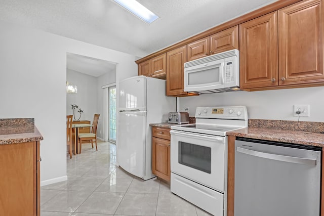 1265 Pine Sage Cir, West Palm Beach, FL 33409 - kitchen with white appliances, brown cabinetry, light tile patterned floors, and dark stone countertops