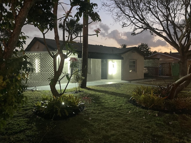 604 W Ocean Ave, Lantana, FL 33462 - back of house at dusk with stucco siding, a yard, and a patio area
