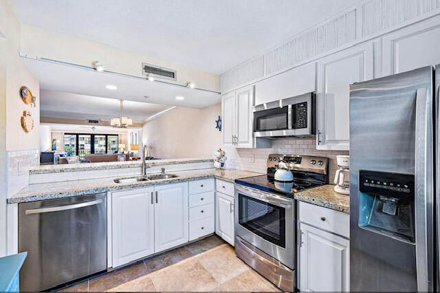 kitchen with appliances with stainless steel finishes, a sink, white cabinetry, and backsplash