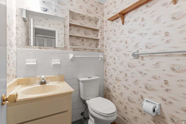 bathroom featuring toilet, wallpapered walls, vanity, and tile walls