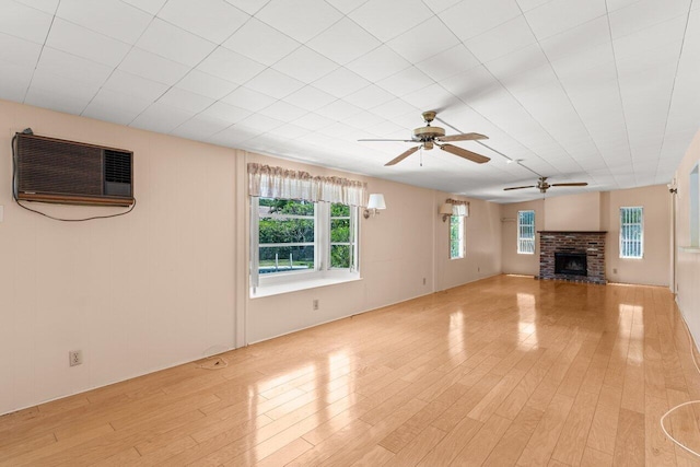 unfurnished living room with ceiling fan, light wood-type flooring, a brick fireplace, and a wall unit AC