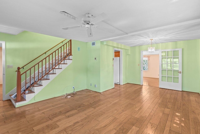 unfurnished living room with wood finished floors, stairs, a chandelier, and a ceiling fan