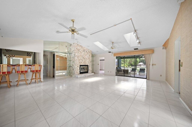 unfurnished living room featuring ceiling fan, a stone fireplace, lofted ceiling, a skylight, and a textured ceiling