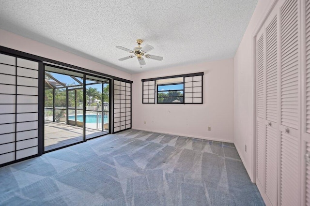 unfurnished bedroom with access to outside, a textured ceiling, carpet floors, multiple windows, and ceiling fan