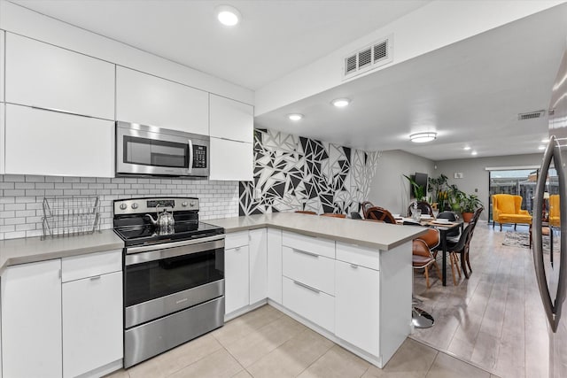 184 NW 115th Ter, Plantation, FL 33325 - kitchen featuring appliances with stainless steel finishes, a peninsula, white cabinets, tasteful backsplash, and recessed lighting