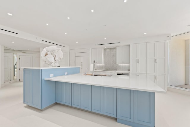 kitchen featuring a sink, white cabinets, light countertops, a spacious island, and backsplash