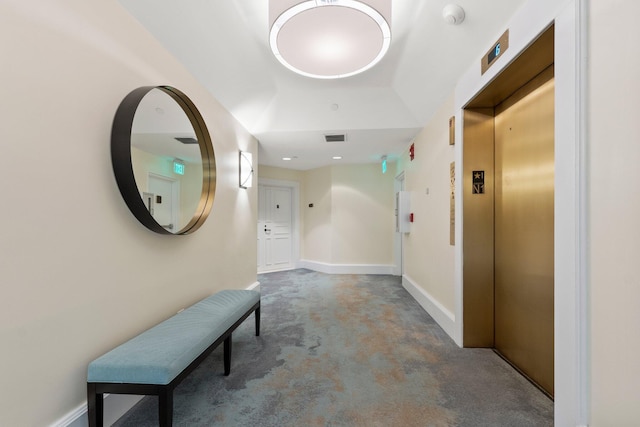 hallway featuring elevator, concrete floors, and baseboards