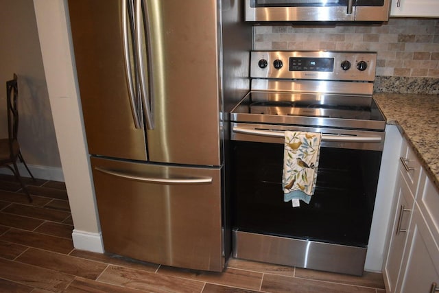 kitchen with appliances with stainless steel finishes, white cabinetry, backsplash, wood finish floors, and light stone counters