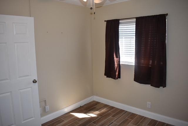 spare room with baseboards, dark wood-type flooring, and a ceiling fan