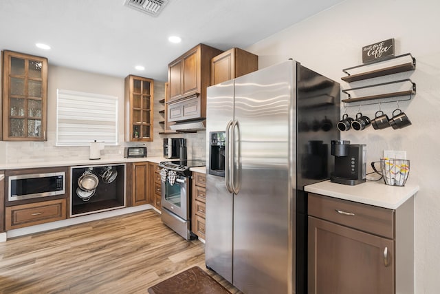 kitchen with stainless steel appliances, backsplash, glass insert cabinets, light wood finished floors, and recessed lighting