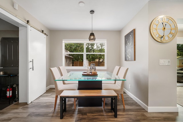 dining space with a barn door, wood finished floors, and baseboards