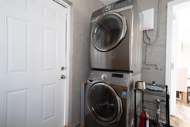 laundry area with stacked washer and clothes dryer and a textured wall
