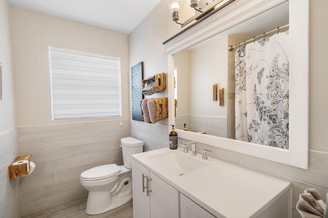 full bath with tile walls, toilet, vanity, a wainscoted wall, and curtained shower